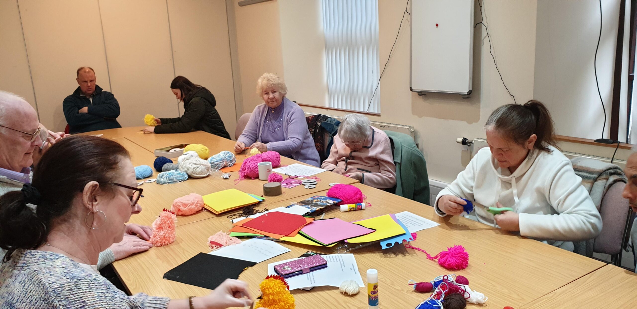 Group of adults sit round table doing crafts
