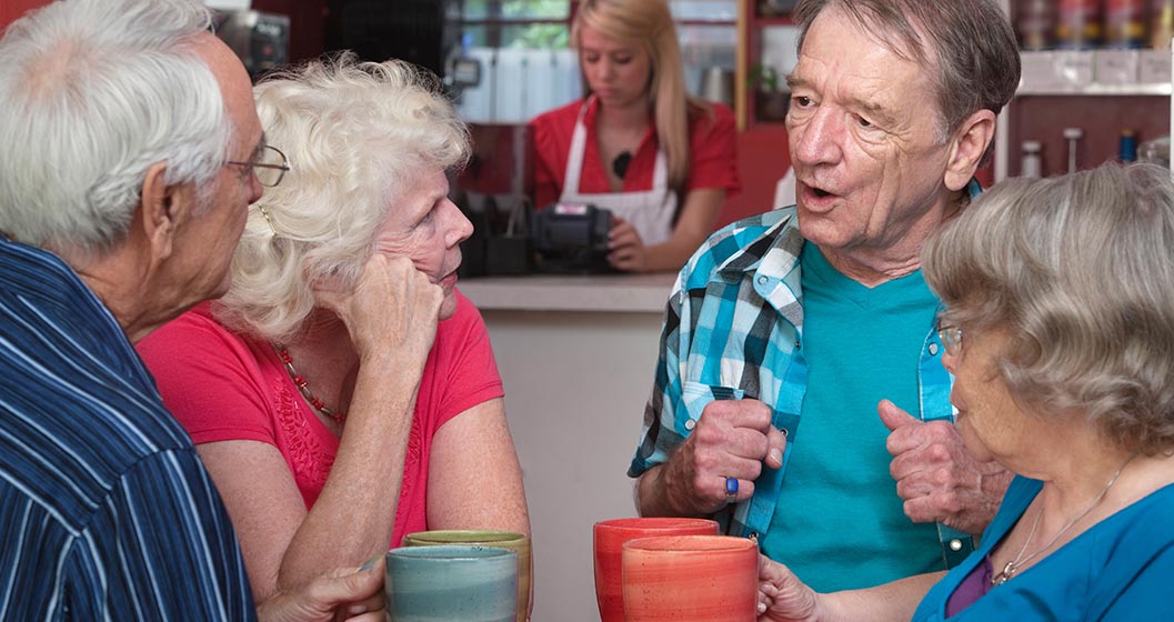 a group of four older people, two men and two women, sit in a cafe chatting