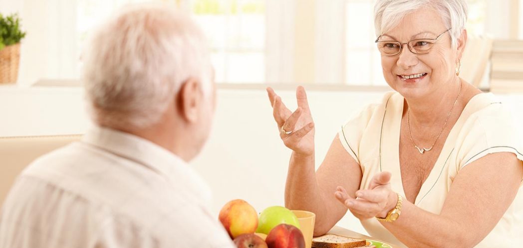 An older woman chats to an older man while sitting at a table