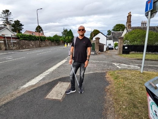 John Dunn stands on the pavement in front of a junction with grass to his left and the road to his right.