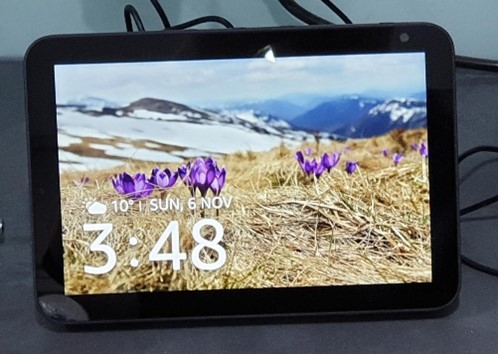 Close up of Amazon Echo Show, a smart tablet with a mountain scene and a large digital clock in the bottom left hand corner