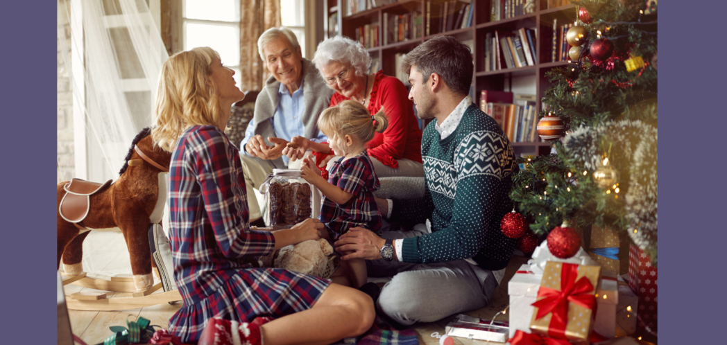 Family of two parents, two grandparents adn two small children sit together opening christmas presents