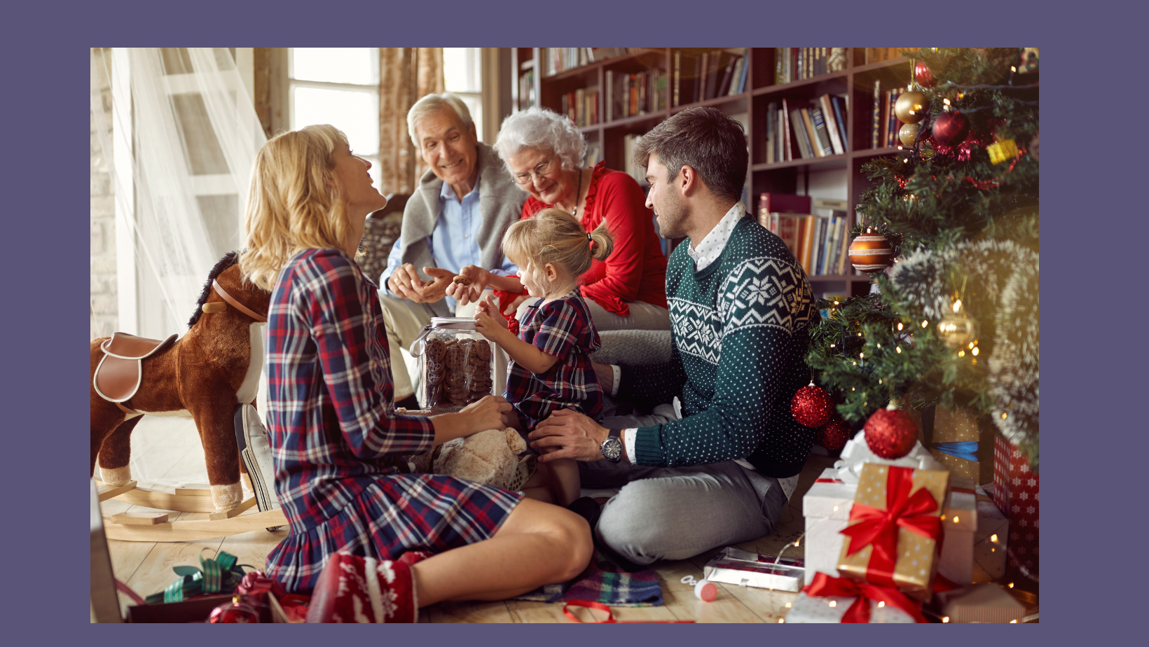 Family of two parents, two grandparents adn two small children sit together opening christmas presents