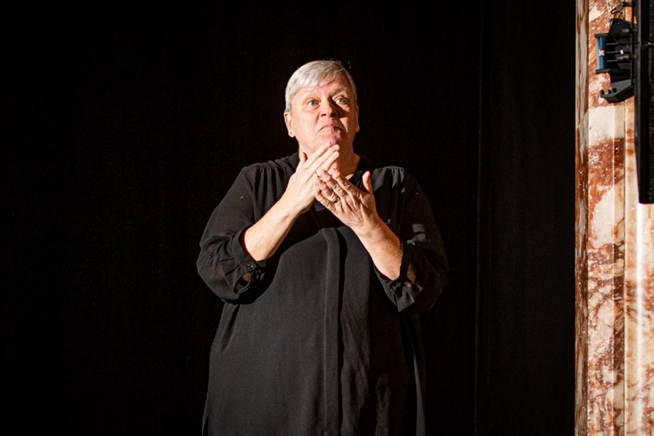 Lelsey Crerar, dressed in black against a black background, interprets at the theatre