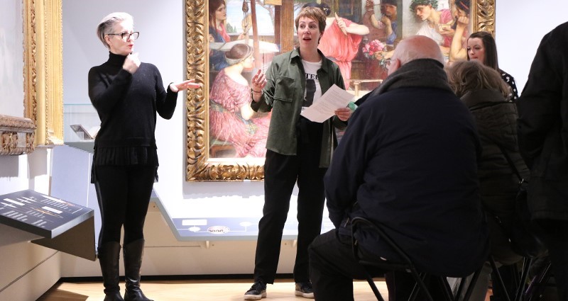 British Sign Language interpreter faces a group of people interpreting what staff member says about the paintings