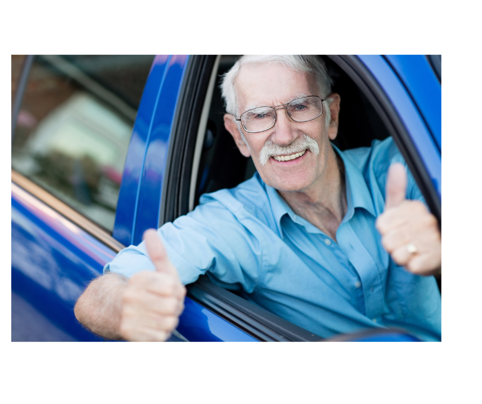 Older man leans out of car window smiling and holding both thumbs up