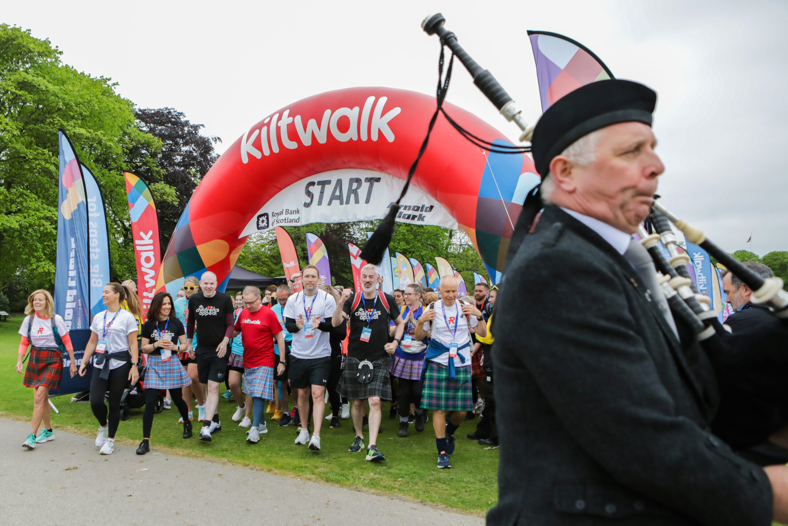 image of people at the Kiltwalk starting line, with a man playing the bagpipes in the foreground