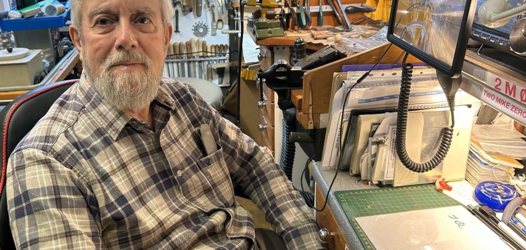 Robin sitting with his jewellery making workshop in behind him, containing lots of tools.