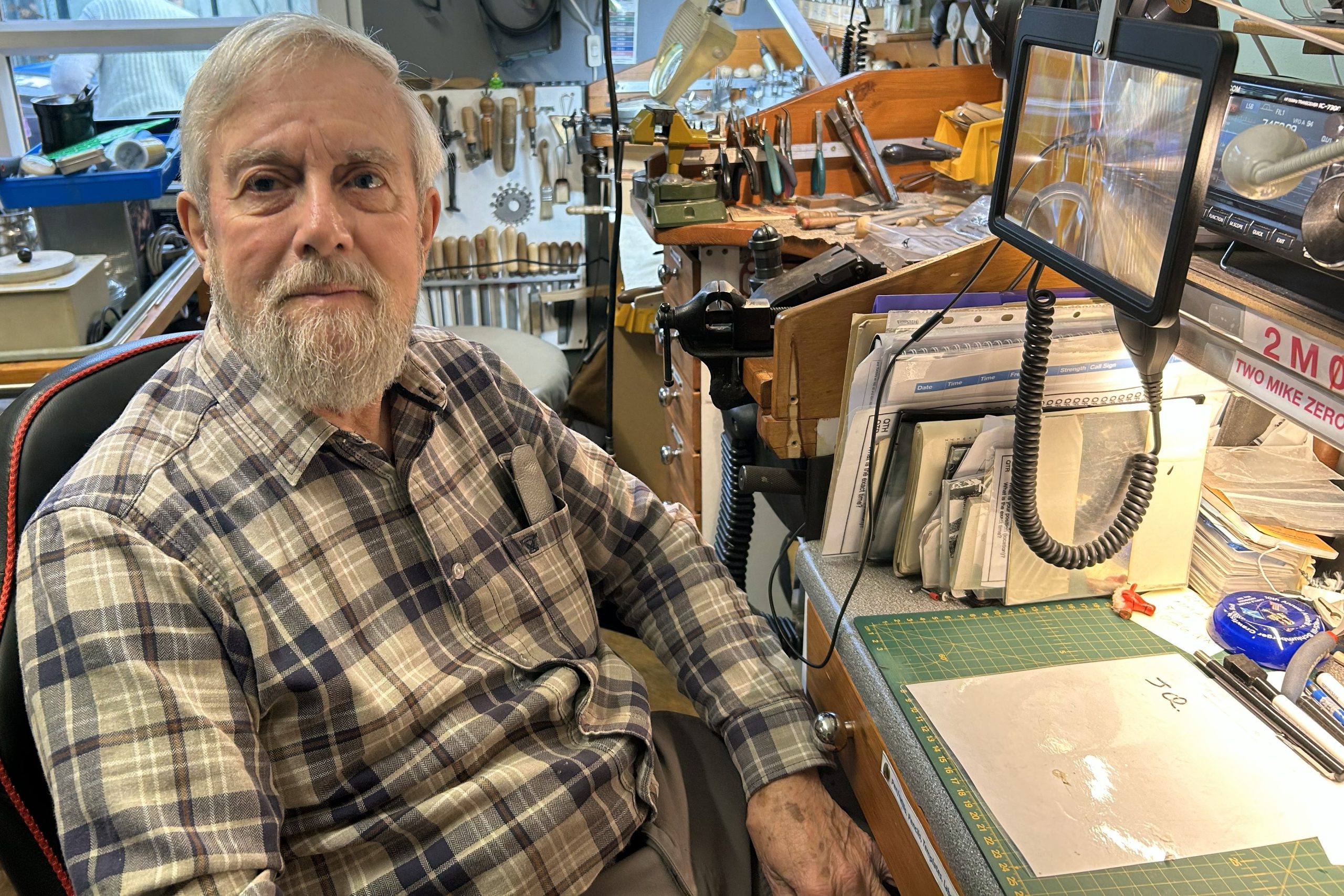 Robin sitting with his jewellery making workshop in behind him, containing lots of tools.